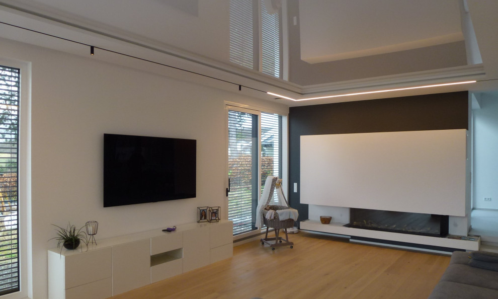 Идея дизайна: огромная открытая гостиная комната в стиле модернизм с белыми стенами, светлым паркетным полом, подвесным камином, телевизором на стене, бежевым полом, многоуровневым потолком и обоями на стенах