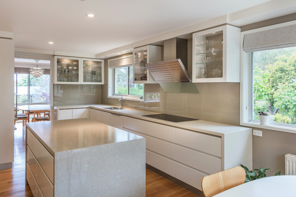 Contemporary l-shaped eat-in kitchen in Sydney with an undermount sink, flat-panel cabinets, white cabinets, beige splashback, panelled appliances, medium hardwood floors, with island, brown floor and white benchtop.