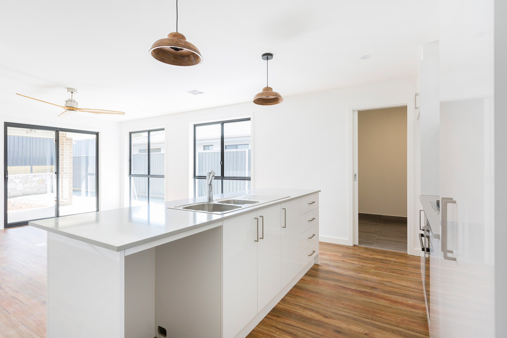 Photo of a small traditional galley kitchen pantry in Canberra - Queanbeyan with a double-bowl sink, flat-panel cabinets, white cabinets, quartz benchtops, grey splashback, porcelain splashback, stainless steel appliances, vinyl floors, with island, brown floor and grey benchtop.
