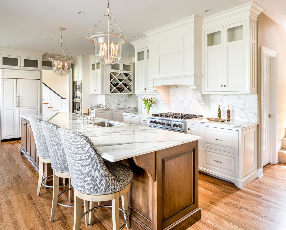 Large traditional l-shaped eat-in kitchen in Philadelphia with an undermount sink, raised-panel cabinets, white cabinets, marble benchtops, white splashback, stone tile splashback, stainless steel appliances, medium hardwood floors, with island, brown floor and white benchtop.