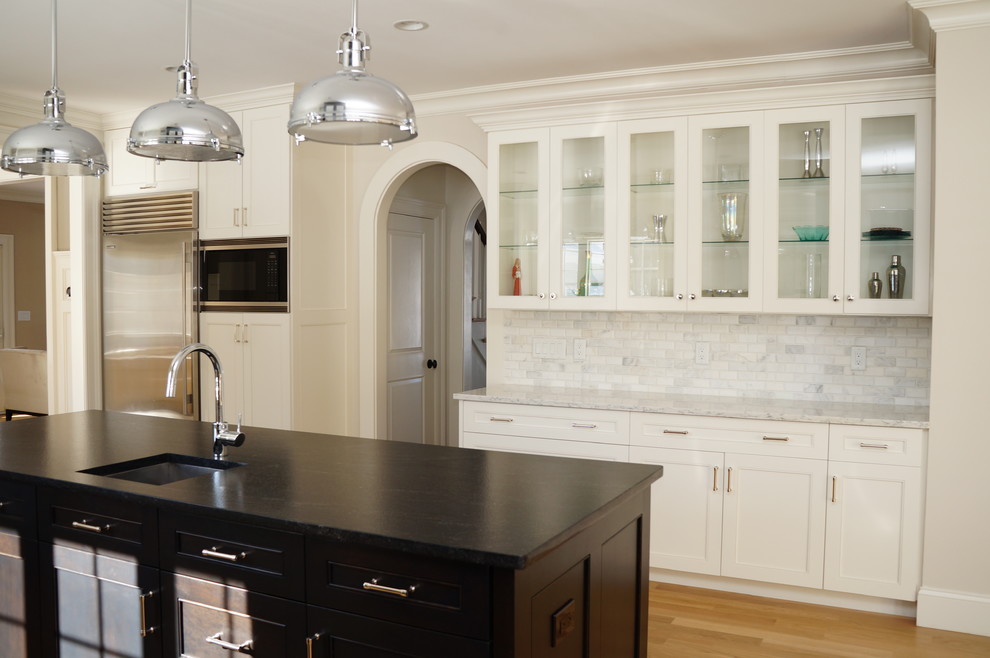 Large transitional l-shaped light wood floor and brown floor kitchen pantry photo in Boston with gray backsplash, stainless steel appliances, an island, an undermount sink, recessed-panel cabinets, white cabinets, solid surface countertops, stone tile backsplash and black countertops