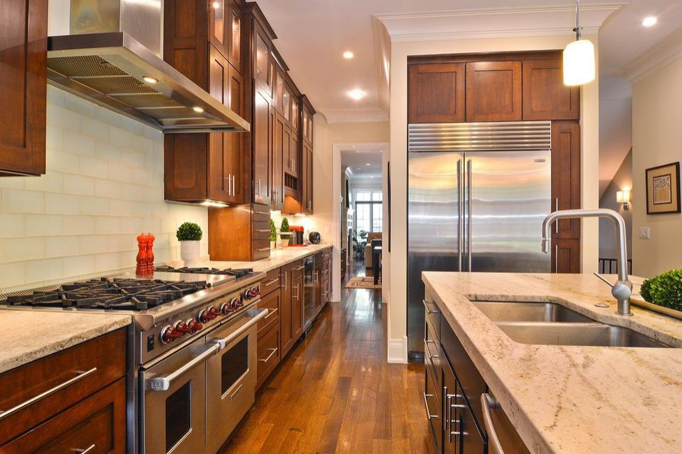 Inspiration for a large transitional open plan kitchen in Chicago with an undermount sink, shaker cabinets, brown cabinets, granite benchtops, white splashback, subway tile splashback, stainless steel appliances, medium hardwood floors, brown floor and beige benchtop.