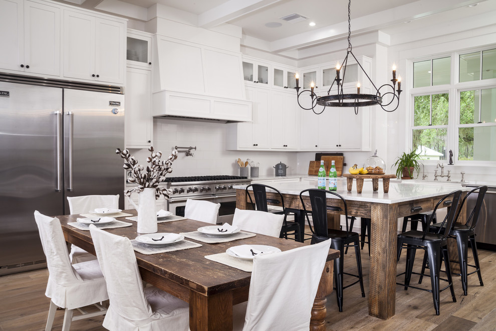 Country l-shaped kitchen in Tampa with shaker cabinets, white cabinets, white splashback, stainless steel appliances, medium hardwood floors, with island and white benchtop.