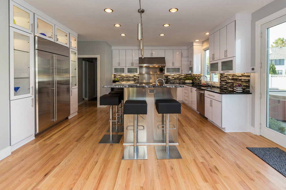 Large trendy u-shaped light wood floor open concept kitchen photo with an undermount sink, flat-panel cabinets, white cabinets, granite countertops, multicolored backsplash, mosaic tile backsplash, stainless steel appliances and an island