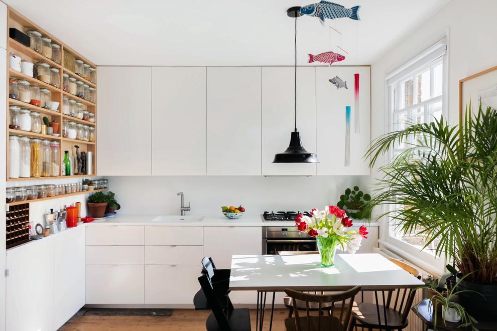 This is an example of a small scandinavian l-shaped eat-in kitchen in London with flat-panel cabinets, white cabinets, stainless steel appliances, no island, white benchtop, an integrated sink, white splashback and medium hardwood floors.