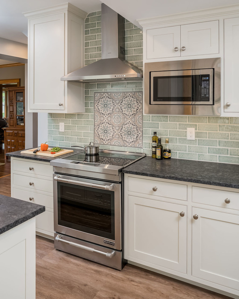 Design ideas for a mid-sized transitional galley eat-in kitchen in Columbus with an undermount sink, shaker cabinets, white cabinets, granite benchtops, green splashback, ceramic splashback, stainless steel appliances, vinyl floors, a peninsula, brown floor and black benchtop.