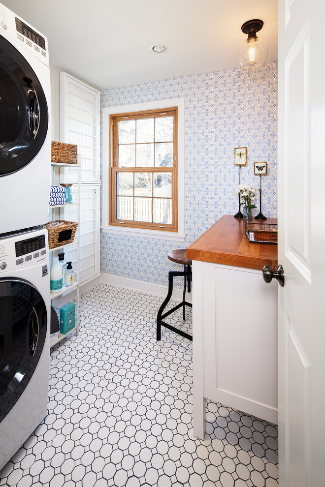 Inspiration for a traditional single-wall dedicated laundry room in Omaha with white cabinets, wood benchtops, blue walls, a stacked washer and dryer, white floor and brown benchtop.