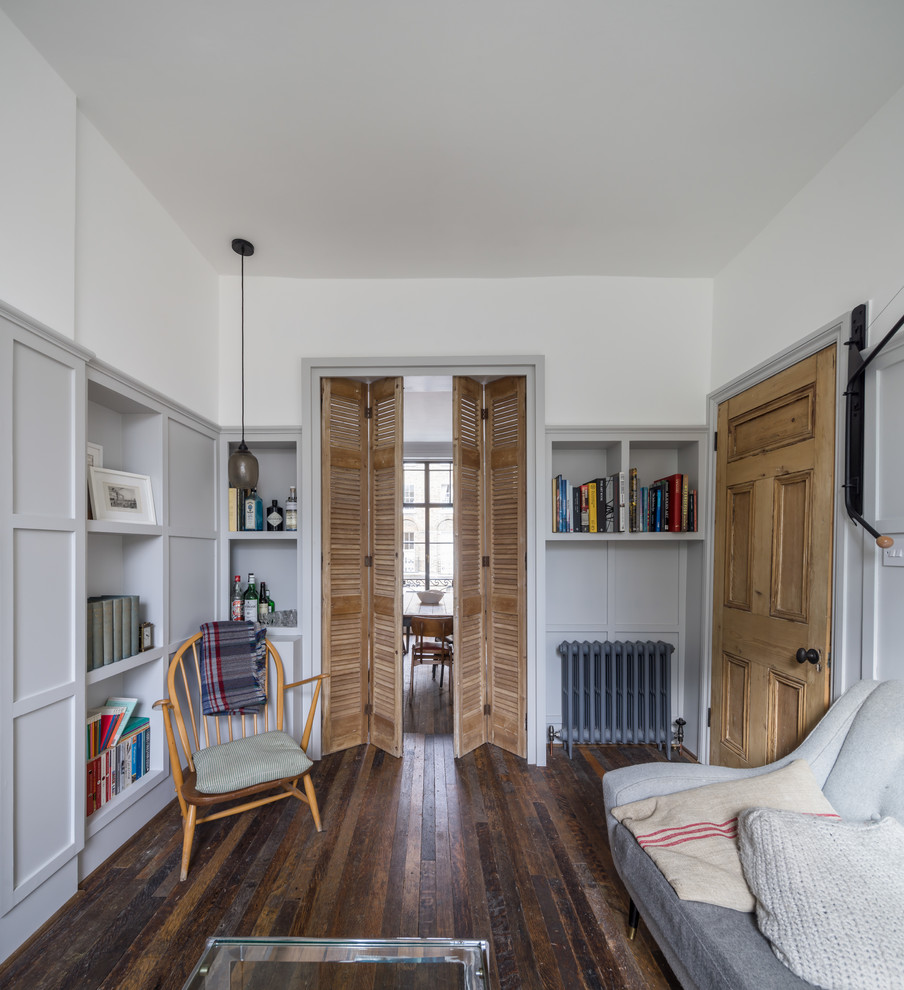 This is an example of a transitional open concept living room in London with a library, grey walls, dark hardwood floors, a standard fireplace and a brick fireplace surround.