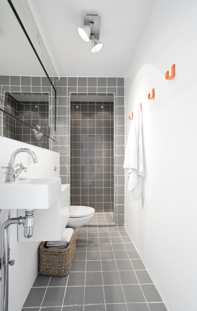 Photo of a mid-sized scandinavian bathroom in Copenhagen with flat-panel cabinets, white cabinets, a wall-mount toilet, gray tile, white walls, ceramic floors, a wall-mount sink and ceramic tile.