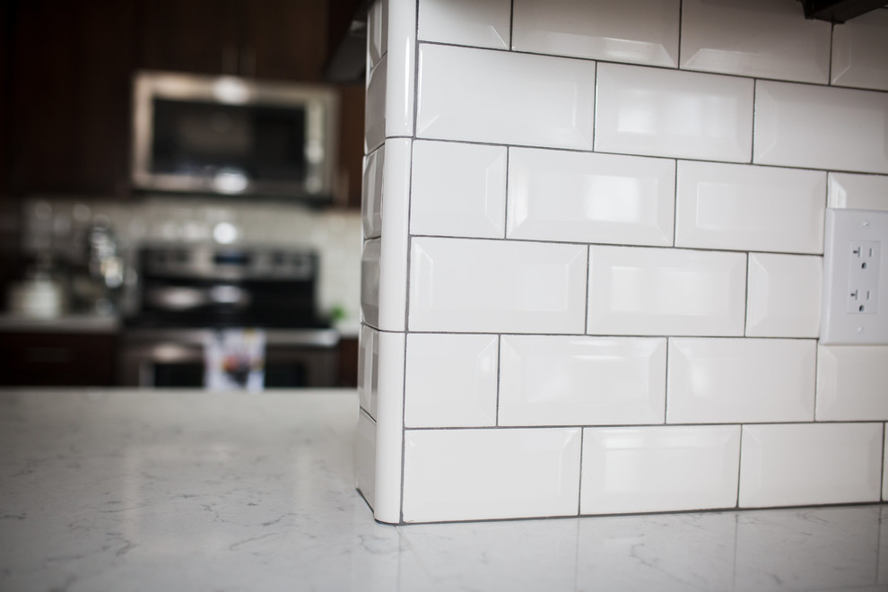 Mid-sized transitional u-shaped medium tone wood floor and brown floor enclosed kitchen photo in Omaha with an undermount sink, shaker cabinets, dark wood cabinets, quartz countertops, white backsplash, subway tile backsplash, stainless steel appliances and a peninsula