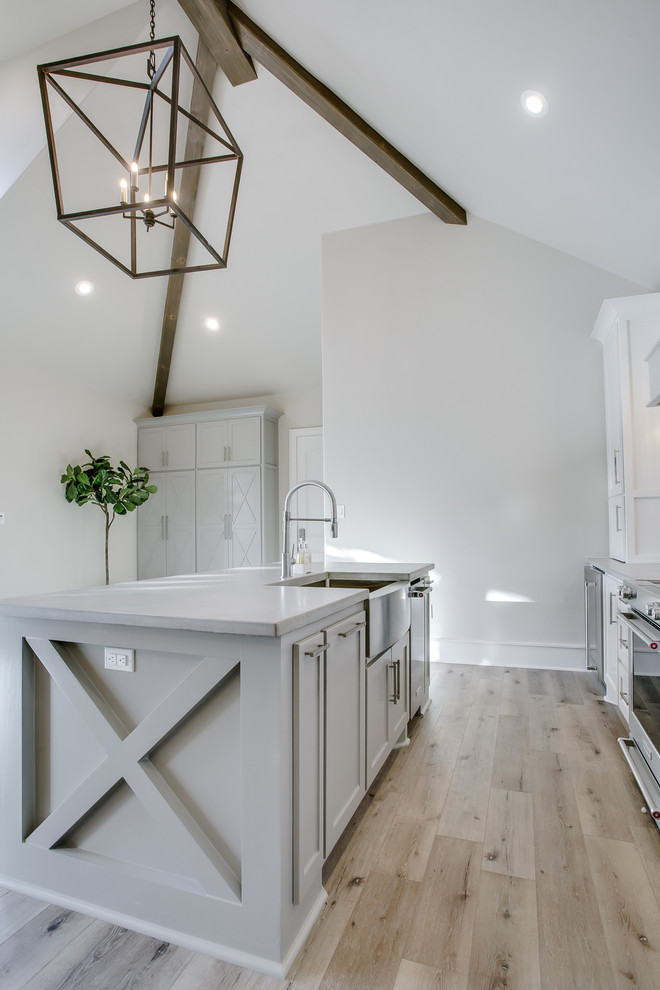 Design ideas for a mid-sized contemporary galley open plan kitchen in Austin with a farmhouse sink, shaker cabinets, white cabinets, solid surface benchtops, white splashback, glass tile splashback, stainless steel appliances, light hardwood floors, with island and beige floor.