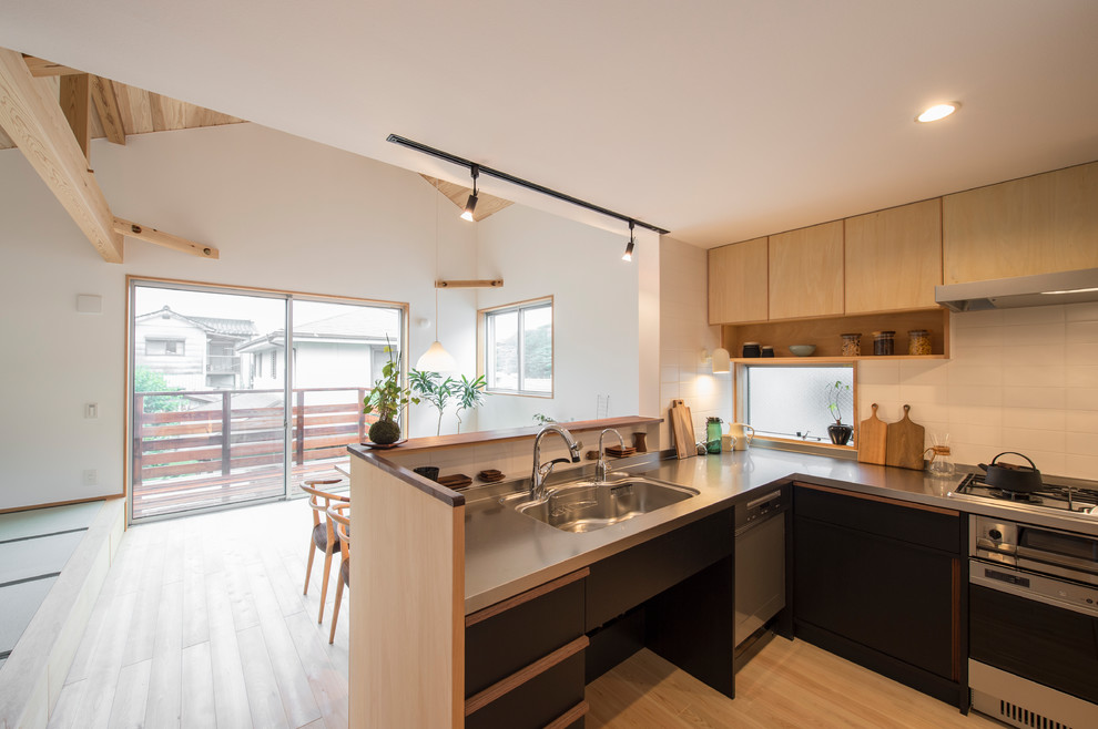 Scandinavian l-shaped kitchen in Yokohama with an integrated sink, black cabinets, stainless steel benchtops, porcelain splashback and stainless steel appliances.