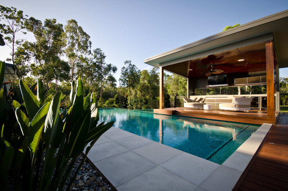 This is an example of a large contemporary side yard custom-shaped infinity pool in Other with a hot tub and concrete pavers.