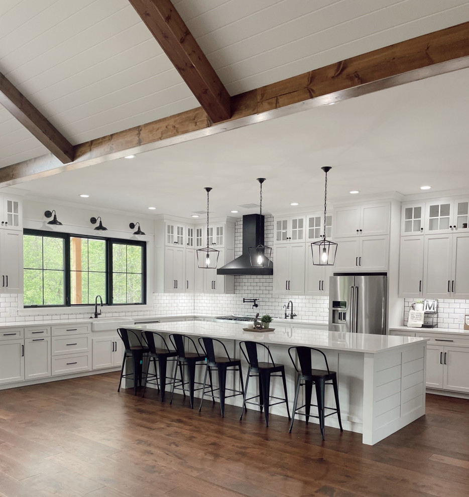 Design ideas for a large modern eat-in kitchen in Chicago with a farmhouse sink, quartz benchtops, white splashback, subway tile splashback, stainless steel appliances, medium hardwood floors, with island, brown floor, white benchtop and exposed beam.