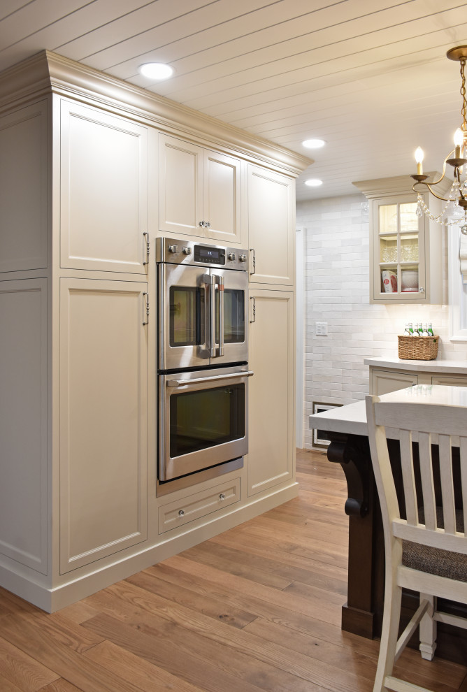 Inspiration for a transitional medium tone wood floor, brown floor and shiplap ceiling eat-in kitchen remodel with shaker cabinets, beige cabinets, quartz countertops, white backsplash, ceramic backsplash, stainless steel appliances, an island and white countertops