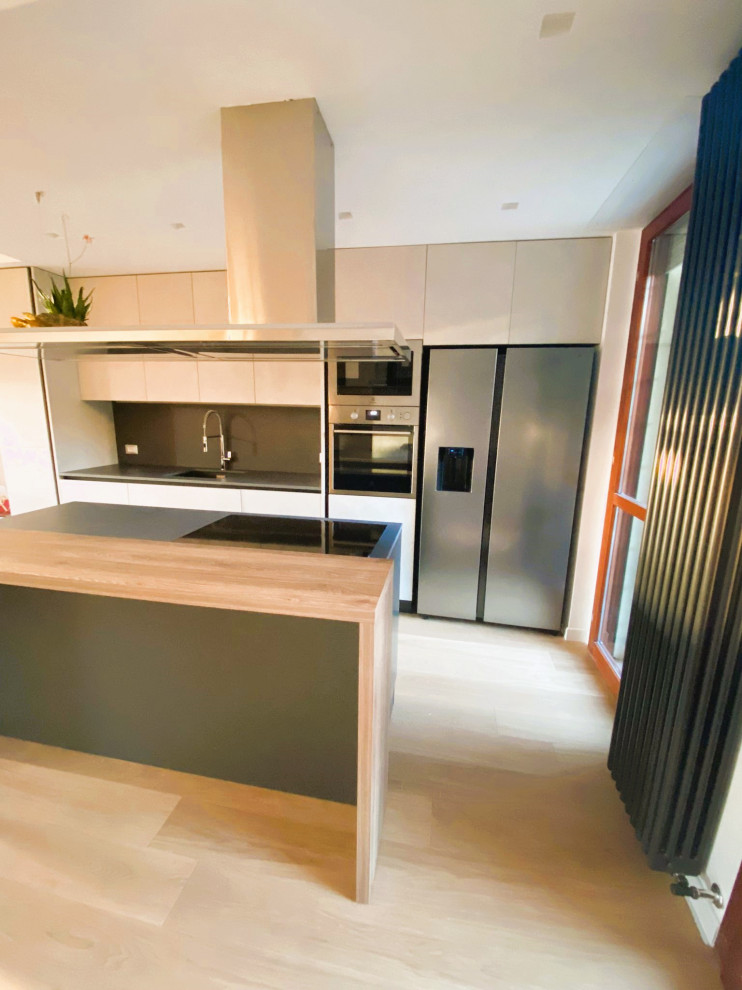 This is an example of a mid-sized modern galley open plan kitchen in Rome with an undermount sink, flat-panel cabinets, white cabinets, quartz benchtops, black splashback, porcelain splashback, stainless steel appliances, light hardwood floors, with island, yellow floor, black benchtop and recessed.