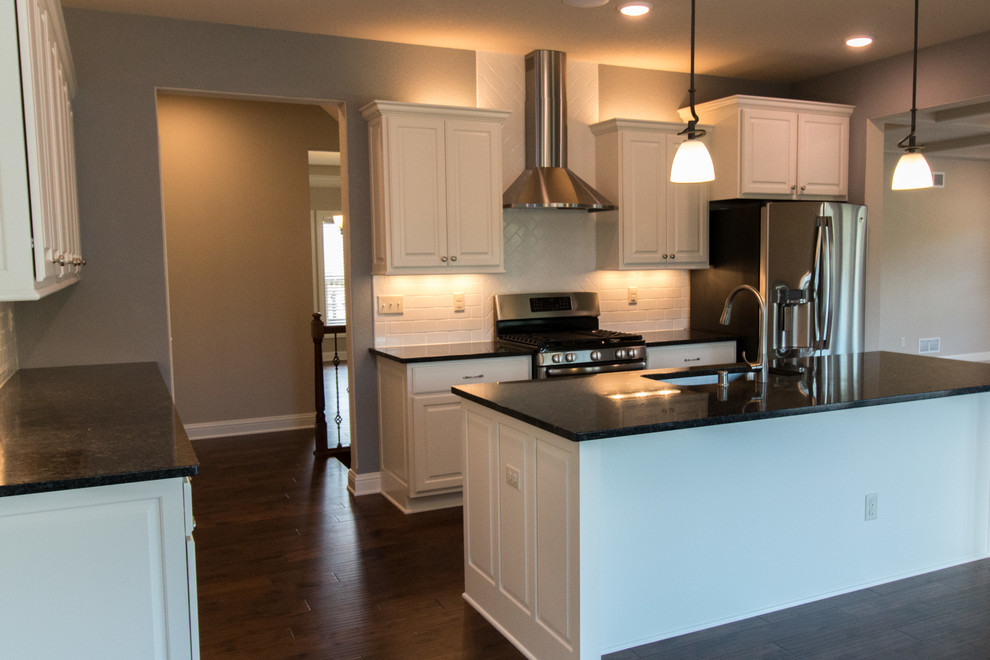 This is an example of a large transitional l-shaped open plan kitchen in Milwaukee with an undermount sink, raised-panel cabinets, white cabinets, granite benchtops, white splashback, subway tile splashback, stainless steel appliances, dark hardwood floors and with island.