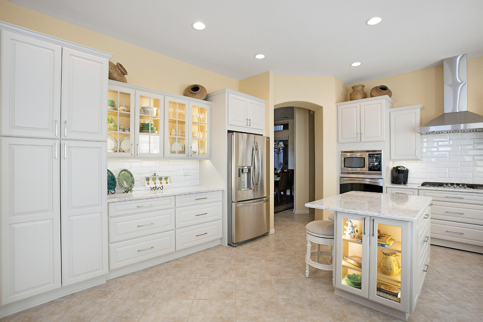 Inspiration for a mid-sized transitional single-wall ceramic tile and beige floor eat-in kitchen remodel with an undermount sink, raised-panel cabinets, white cabinets, quartz countertops, white backsplash, porcelain backsplash, stainless steel appliances and an island