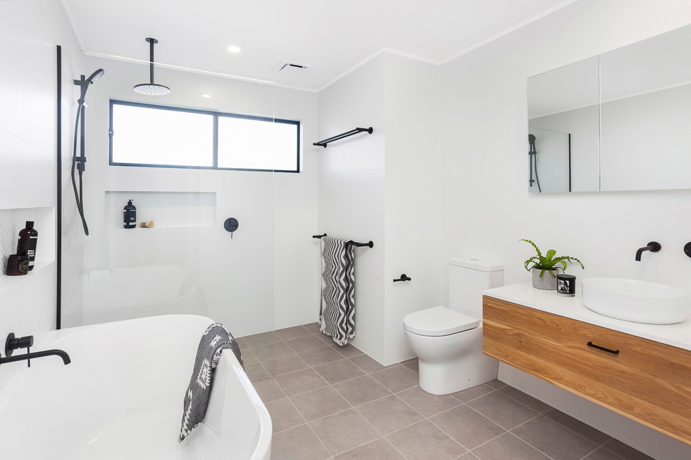 Inspiration for a contemporary master bathroom in Wollongong with flat-panel cabinets, medium wood cabinets, a freestanding tub, a curbless shower, a two-piece toilet, white walls, a vessel sink, grey floor, an open shower and white benchtops.