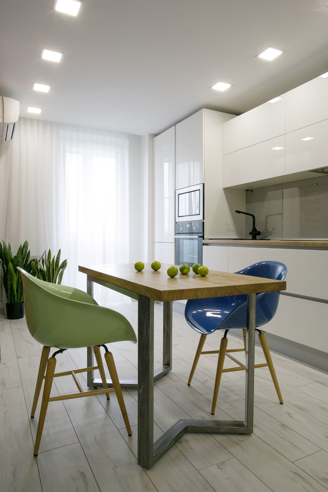 This is an example of a mid-sized contemporary single-wall kitchen in Other with flat-panel cabinets, white cabinets, laminate benchtops, grey splashback, glass sheet splashback, stainless steel appliances, no island and light hardwood floors.