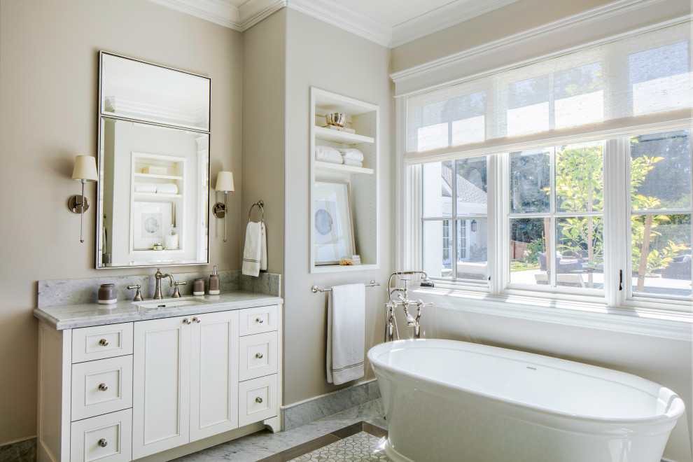 Inspiration for an expansive beach style master bathroom in San Francisco with white cabinets, a freestanding tub, beige walls, marble floors, an undermount sink, marble benchtops, grey floor, grey benchtops, a niche, a double vanity, a built-in vanity and recessed-panel cabinets.