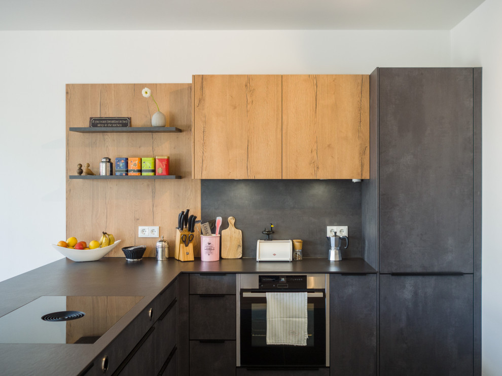 Photo of a small contemporary l-shaped kitchen in Cologne with flat-panel cabinets, grey cabinets, black splashback, panelled appliances, a peninsula and black benchtop.