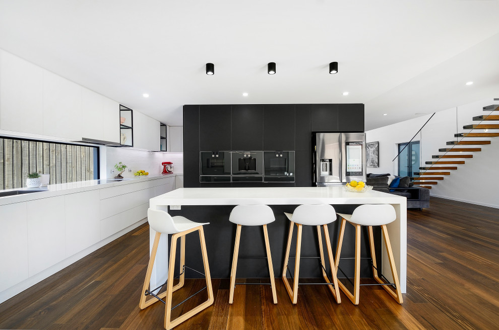 This is an example of a contemporary l-shaped kitchen in Melbourne with flat-panel cabinets, stainless steel appliances, dark hardwood floors, with island, brown floor and white benchtop.