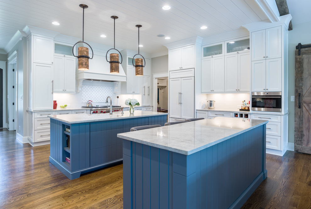 Large transitional l-shaped medium tone wood floor eat-in kitchen photo in Atlanta with a farmhouse sink, shaker cabinets, white cabinets, quartzite countertops, white backsplash, white appliances and two islands