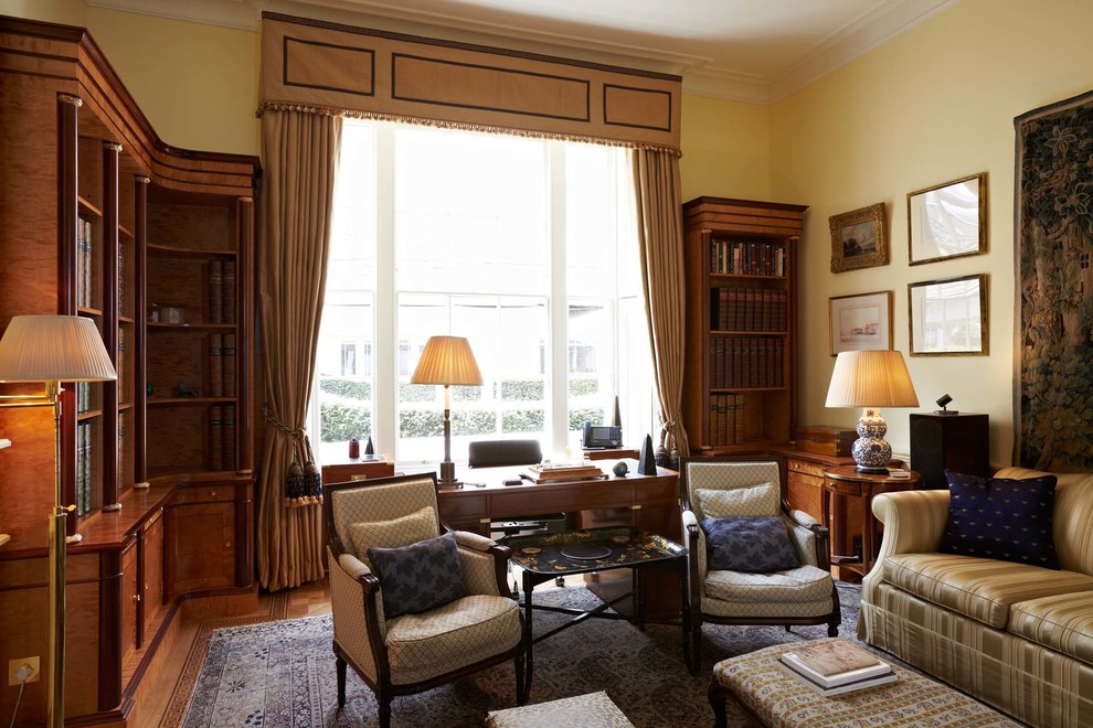 Photo of a large traditional home office in London with yellow walls and medium hardwood floors.
