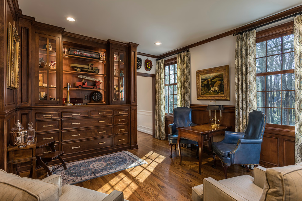 Large traditional study room in Other with beige walls, medium hardwood floors, a standard fireplace, a wood fireplace surround, a built-in desk and brown floor.