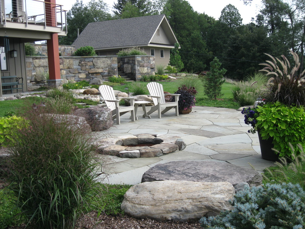 Expansive country backyard full sun garden in Burlington with a fire feature and natural stone pavers for summer.