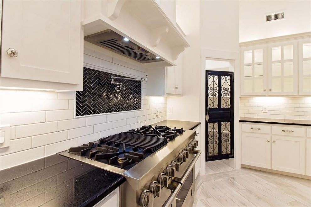 Mid-sized transitional l-shaped eat-in kitchen in Houston with a triple-bowl sink, shaker cabinets, white cabinets, quartzite benchtops, white splashback, ceramic splashback, stainless steel appliances, porcelain floors, with island, multi-coloured floor, black benchtop and coffered.