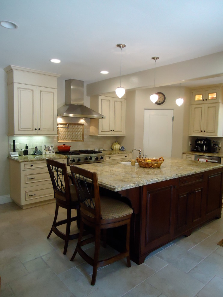 Mid-sized traditional u-shaped eat-in kitchen in Los Angeles with a farmhouse sink, raised-panel cabinets, white cabinets, granite benchtops, beige splashback, limestone splashback, stainless steel appliances, porcelain floors, with island, beige floor and multi-coloured benchtop.