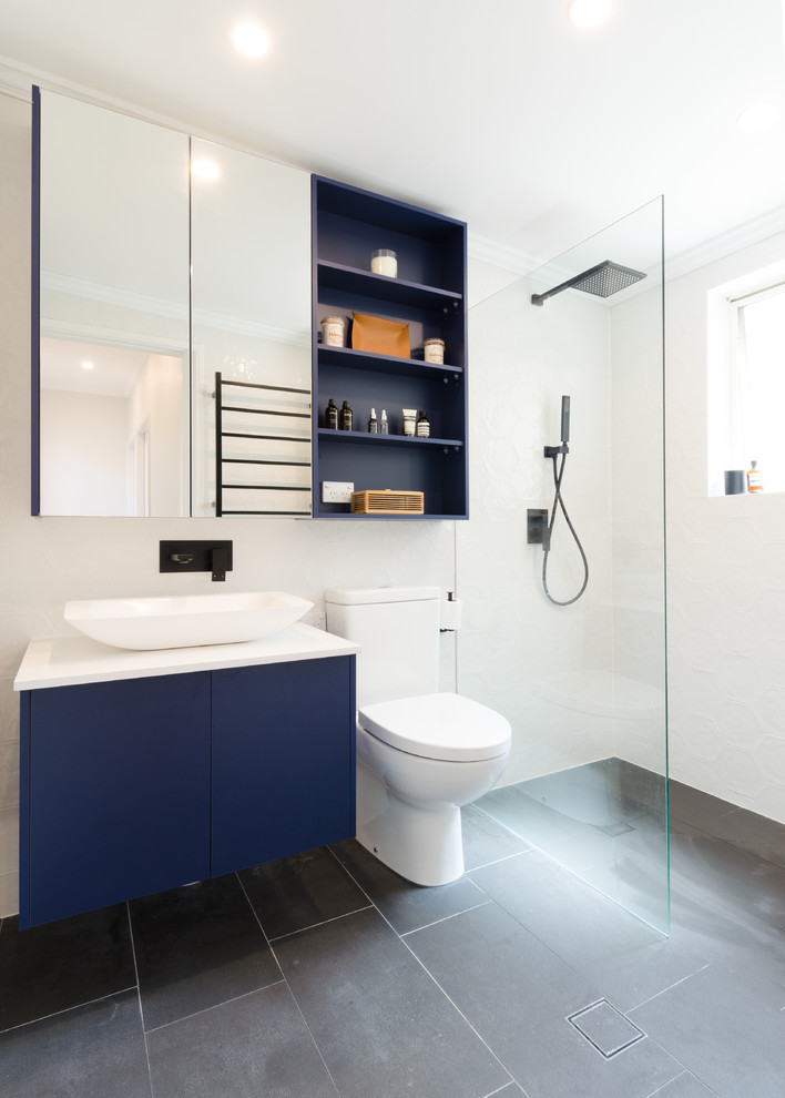 This is an example of a small contemporary kids bathroom in Sydney with flat-panel cabinets, blue cabinets, an open shower, a one-piece toilet, gray tile, ceramic tile, white walls, ceramic floors, a trough sink and engineered quartz benchtops.
