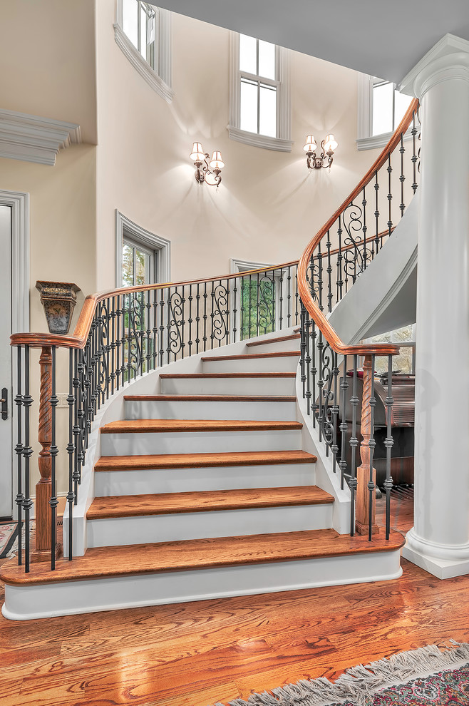Large traditional wood curved staircase in Other with painted wood risers.