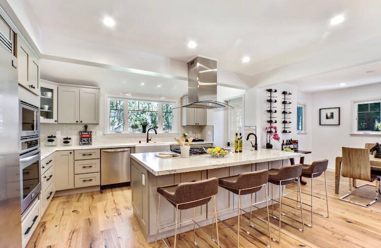 Large transitional l-shaped eat-in kitchen in Los Angeles with a farmhouse sink, shaker cabinets, grey cabinets, marble benchtops, white splashback, stainless steel appliances, light hardwood floors, with island, beige floor, ceramic splashback and white benchtop.