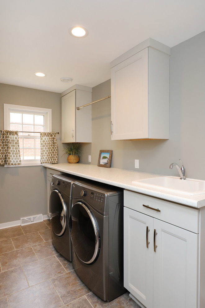 Mid-sized traditional galley utility room in Grand Rapids with an integrated sink, shaker cabinets, white cabinets, laminate benchtops, grey walls, laminate floors, a side-by-side washer and dryer and brown floor.