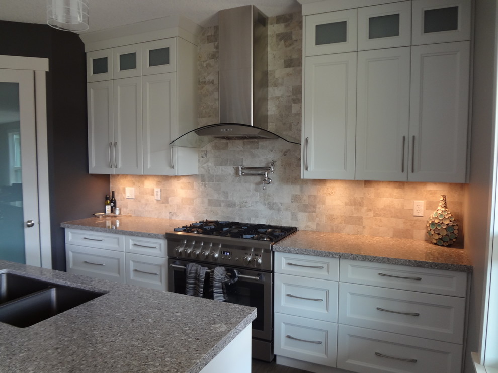 Example of a small transitional single-wall laminate floor and gray floor open concept kitchen design with an undermount sink, shaker cabinets, white cabinets, gray backsplash, travertine backsplash, stainless steel appliances, an island, gray countertops and quartz countertops