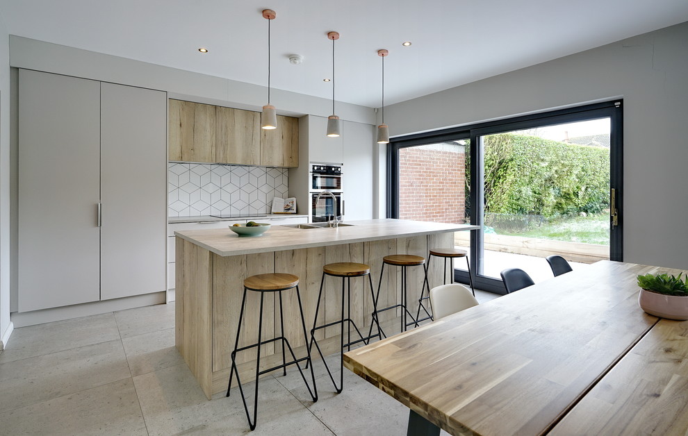 Mid-sized contemporary single-wall open plan kitchen in Belfast with a drop-in sink, flat-panel cabinets, beige cabinets, laminate benchtops, white splashback, ceramic splashback, black appliances, cement tiles, with island, grey floor and grey benchtop.