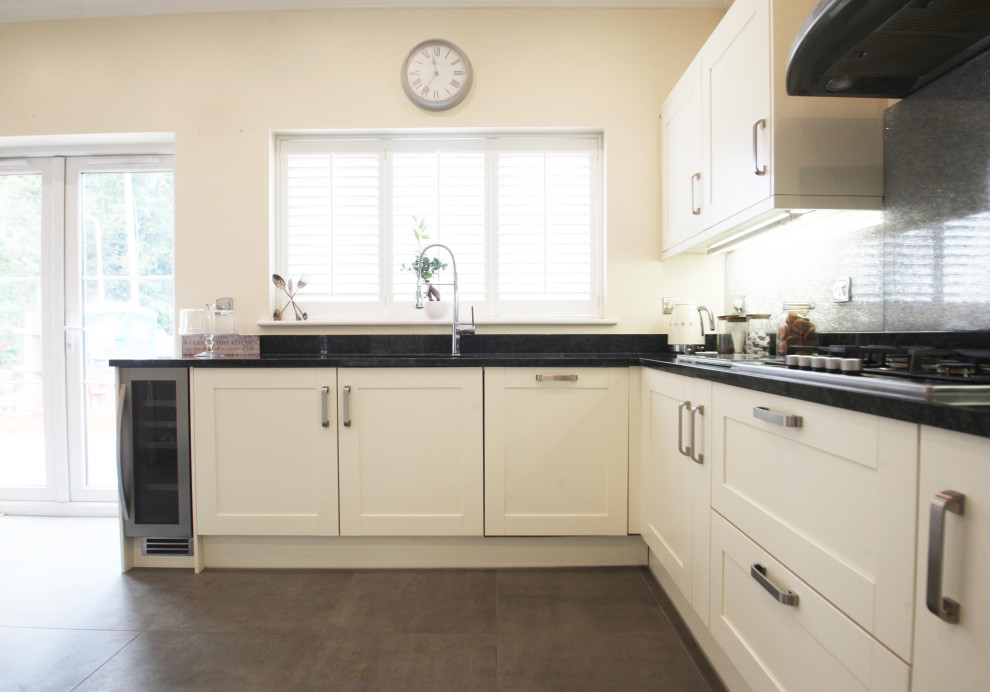 This is an example of a mid-sized traditional u-shaped separate kitchen in Cheshire with a drop-in sink, shaker cabinets, white cabinets, granite benchtops, black splashback, glass tile splashback, stainless steel appliances, slate floors, no island, grey floor and black benchtop.