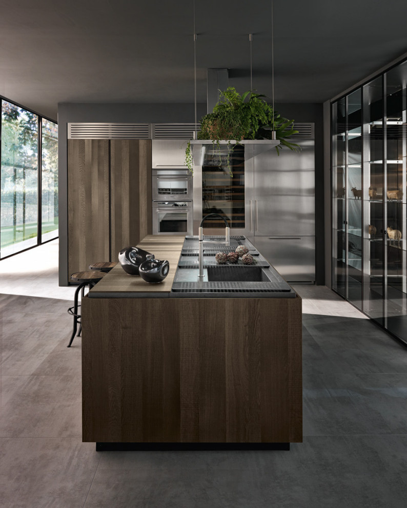 This is an example of a large modern l-shaped kitchen/diner in Los Angeles with a triple-bowl sink, glass-front cabinets, medium wood cabinets, wood worktops, concrete flooring, an island and brown worktops.