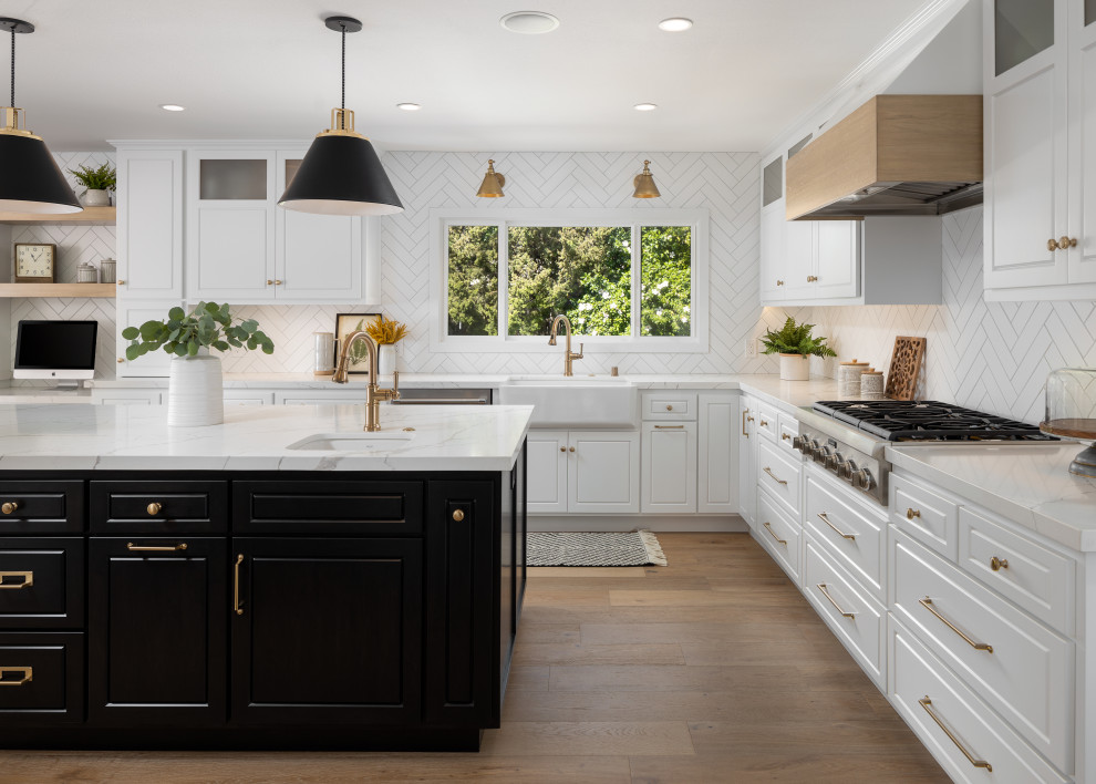 Inspiration for a transitional l-shaped kitchen in Orange County with a farmhouse sink, raised-panel cabinets, white cabinets, white splashback, stainless steel appliances, light hardwood floors, with island and white benchtop.
