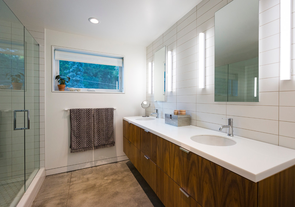 Inspiration for a mid-sized contemporary master bathroom in Cincinnati with flat-panel cabinets, medium wood cabinets, an alcove shower, a one-piece toilet, white tile, ceramic tile, white walls, concrete floors, an undermount sink and solid surface benchtops.