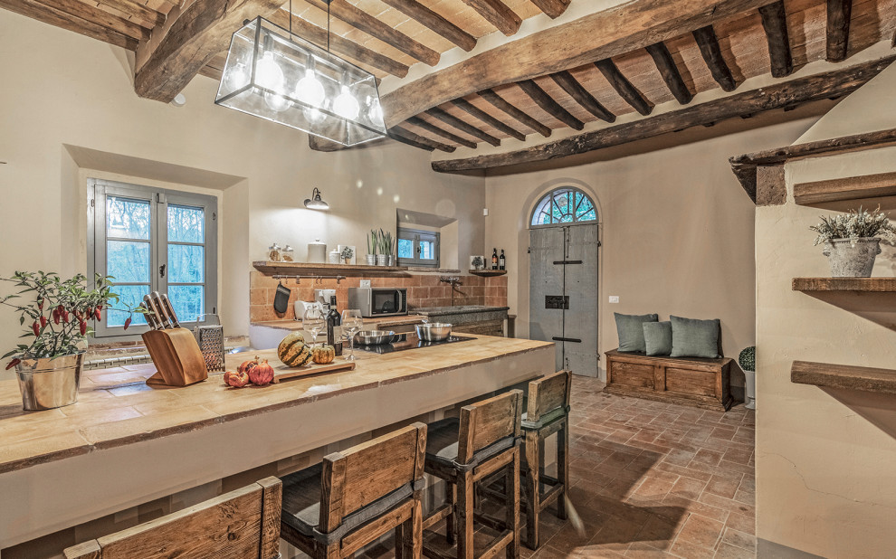 This is an example of a large country galley eat-in kitchen in Florence with a farmhouse sink, beaded inset cabinets, distressed cabinets, tile benchtops, stainless steel appliances, brick floors, with island, orange floor, orange benchtop and exposed beam.