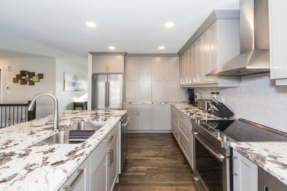 Photo of a mid-sized transitional l-shaped eat-in kitchen in Edmonton with an undermount sink, shaker cabinets, grey cabinets, granite benchtops, grey splashback, ceramic splashback, stainless steel appliances, dark hardwood floors, with island, grey floor and multi-coloured benchtop.