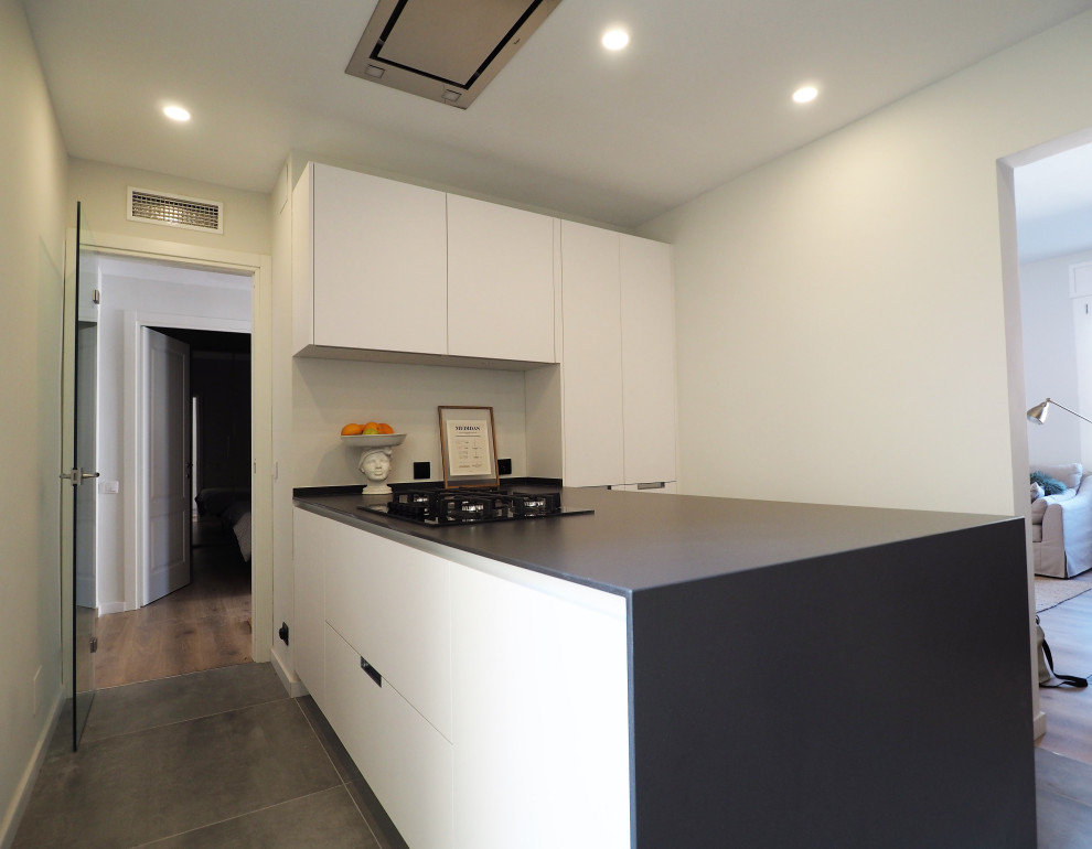Photo of a mid-sized contemporary single-wall open plan kitchen in Barcelona with an integrated sink, shaker cabinets, white cabinets, quartz benchtops, black splashback, stainless steel appliances, with island and black benchtop.