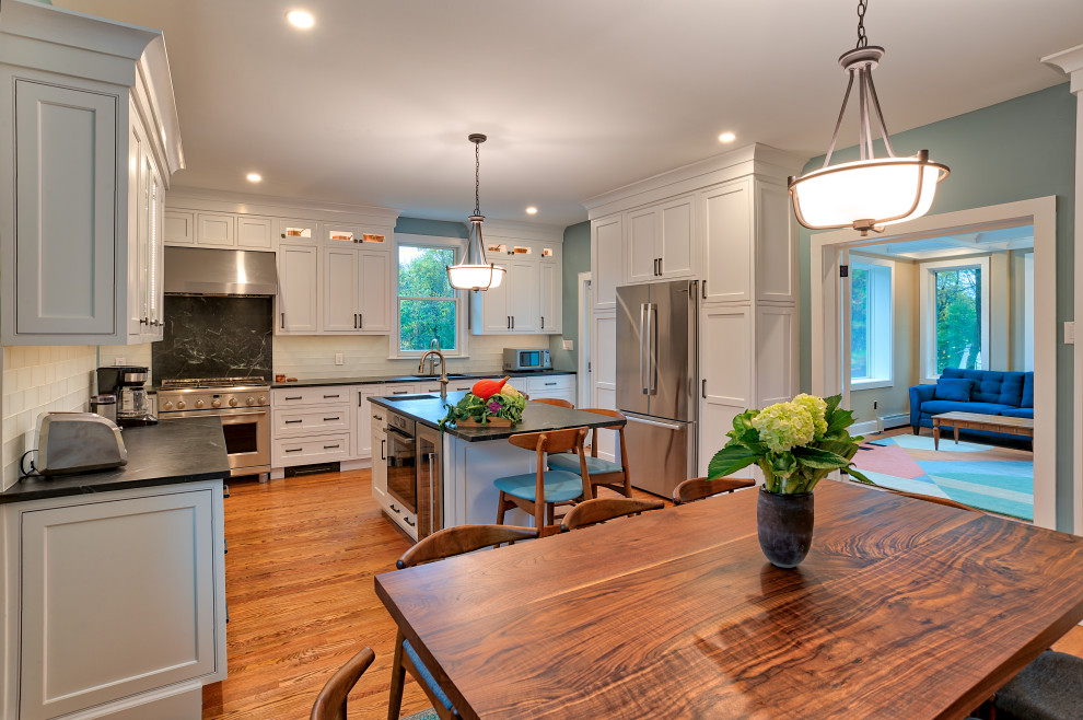 Large traditional l-shaped eat-in kitchen in Philadelphia with an undermount sink, white cabinets, soapstone benchtops, white splashback, subway tile splashback, stainless steel appliances, medium hardwood floors, with island, brown floor, black benchtop and coffered.