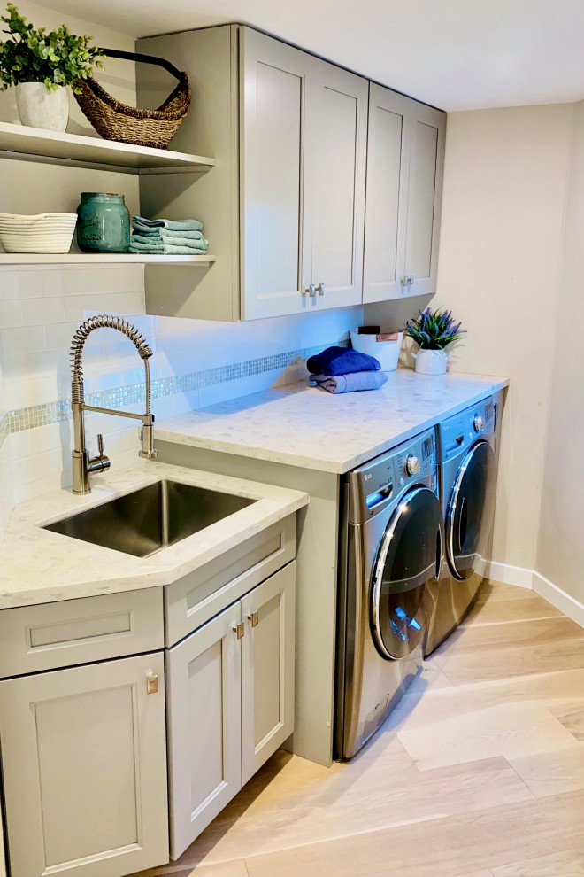 Inspiration for a mid-sized transitional dedicated laundry room in San Francisco with an undermount sink, shaker cabinets, grey cabinets, quartz benchtops, white splashback, glass tile splashback, beige walls, light hardwood floors, a side-by-side washer and dryer and white benchtop.