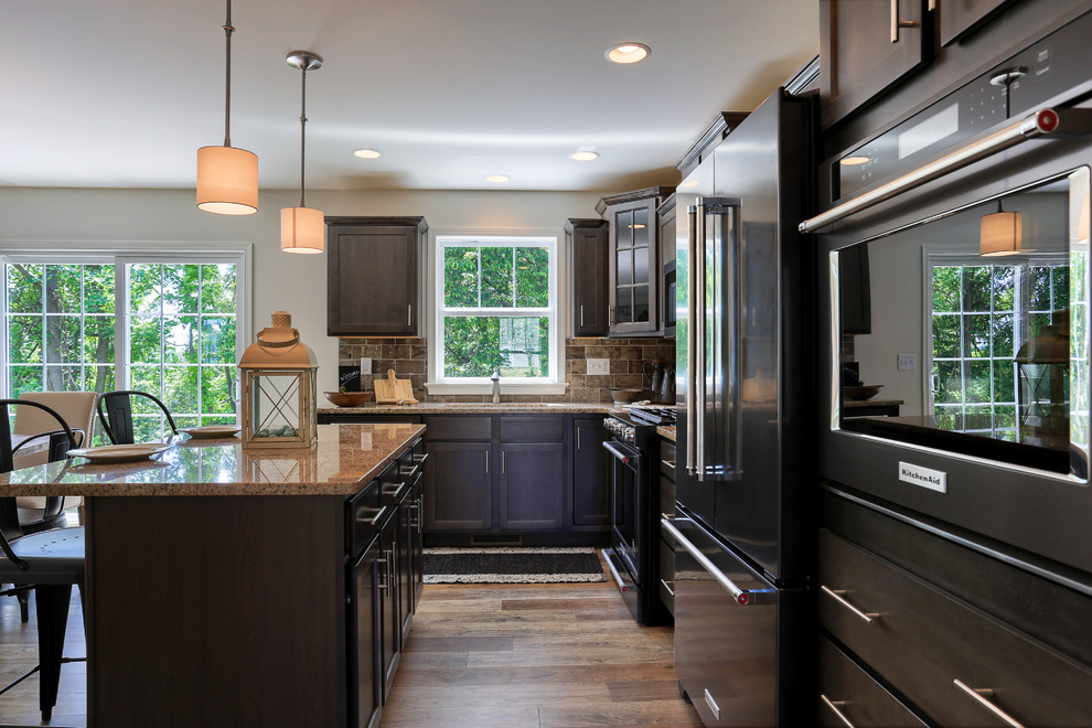 Example of a mid-sized transitional l-shaped medium tone wood floor and brown floor open concept kitchen design with a single-bowl sink, recessed-panel cabinets, dark wood cabinets, granite countertops, gray backsplash, stainless steel appliances and an island