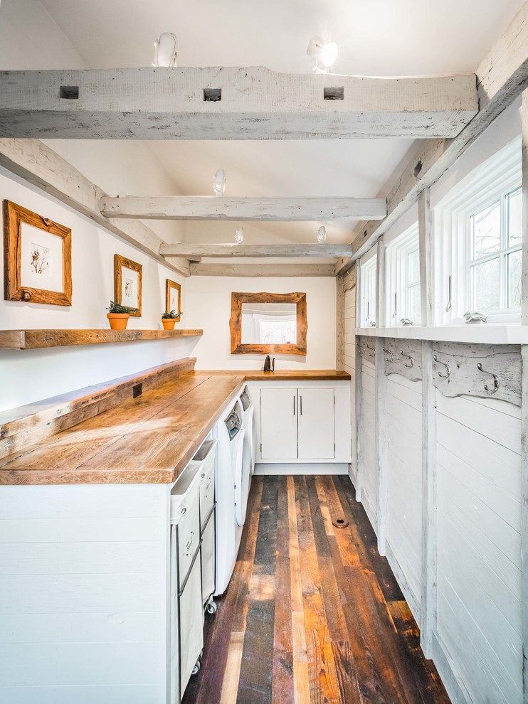 Inspiration for a country l-shaped dedicated laundry room in New York with flat-panel cabinets, white cabinets, wood benchtops, white walls, dark hardwood floors, a side-by-side washer and dryer, brown floor and brown benchtop.